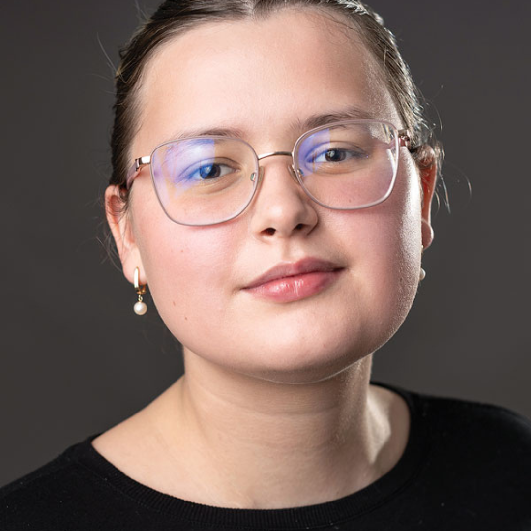 Keira smiles for a close-up professional headshot in front of a dark grey background.