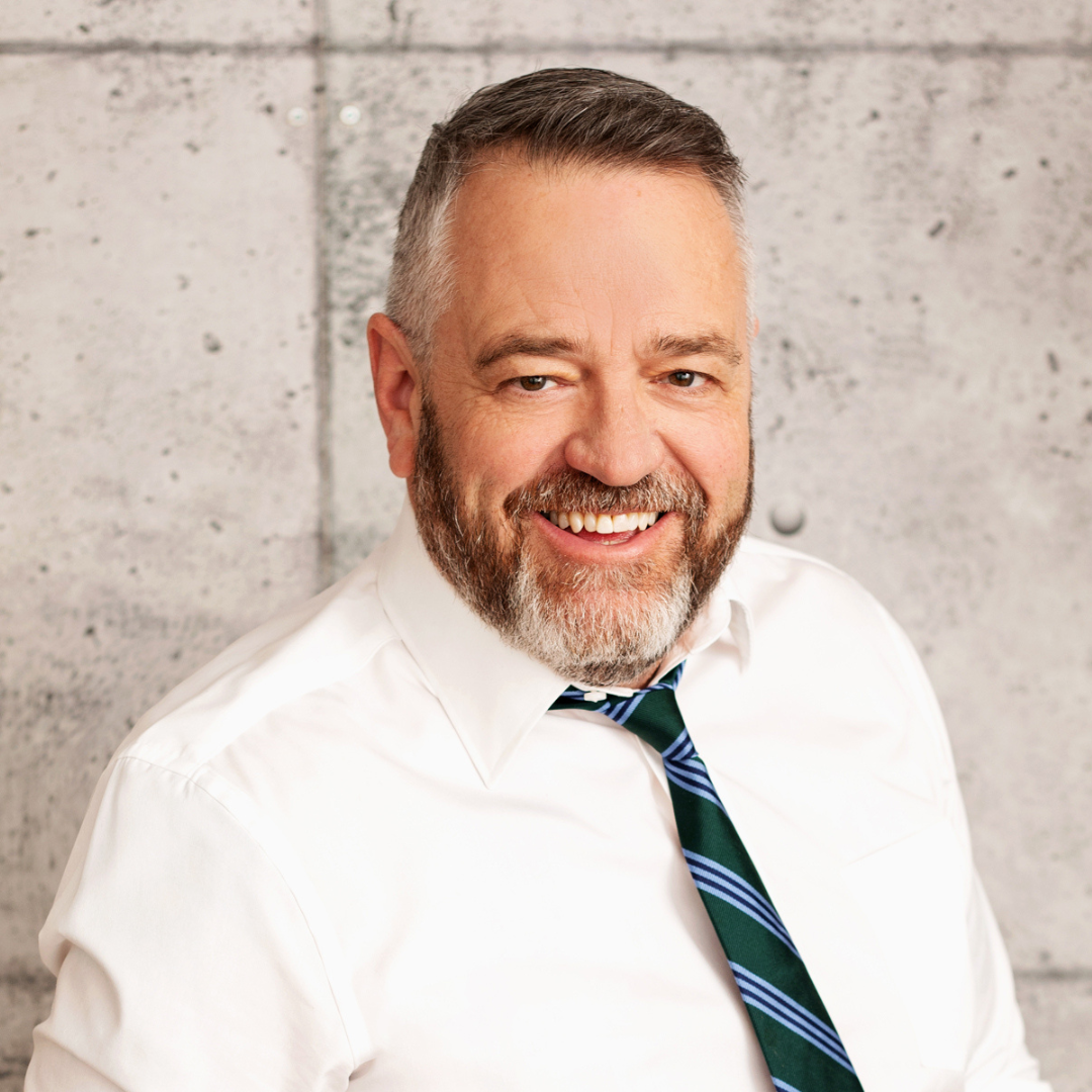 Brad Ross is smiling for a headshot in front of a beige wall. 