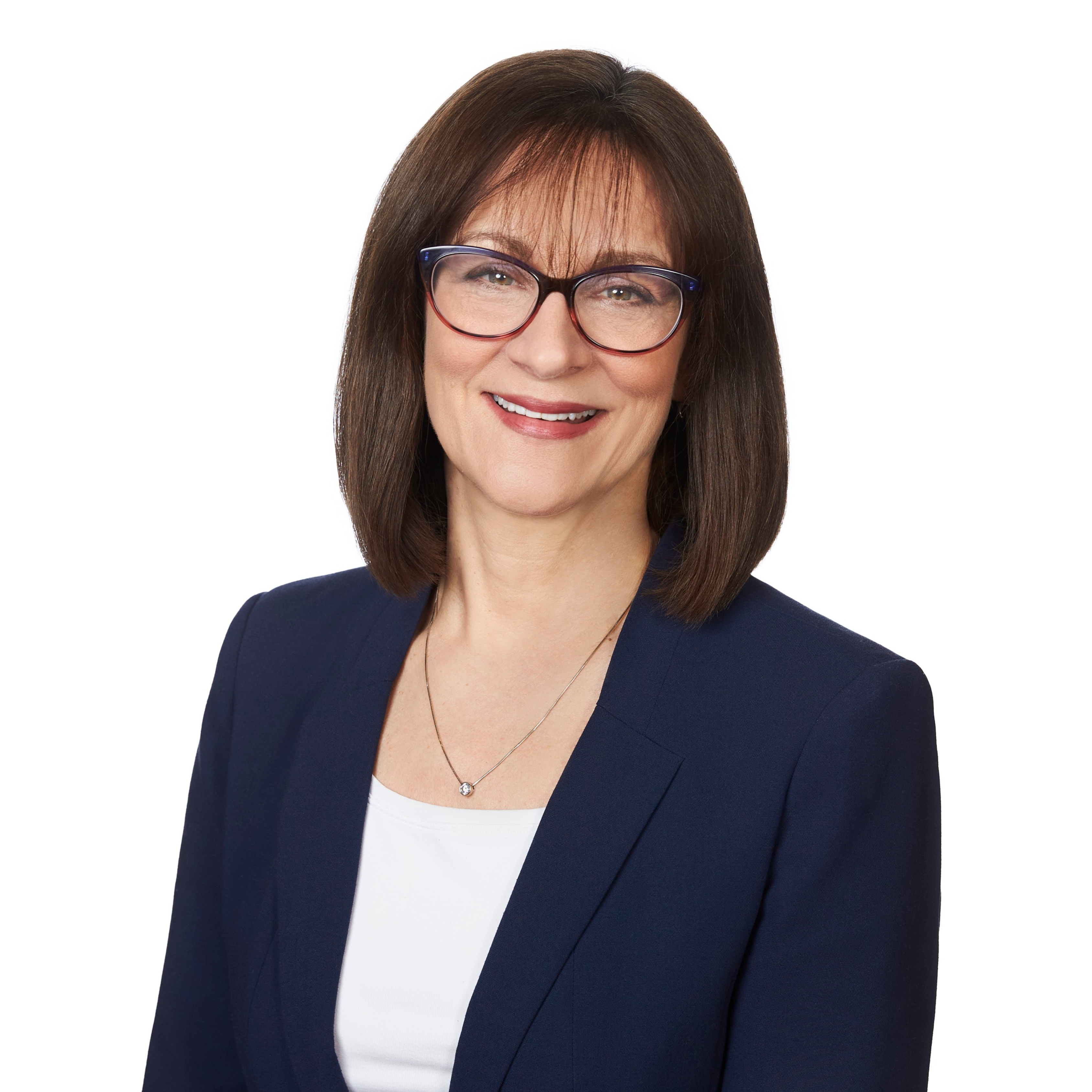 Carole is in a blue blazor standing in front of a white background as she smiles for her professional headshot.