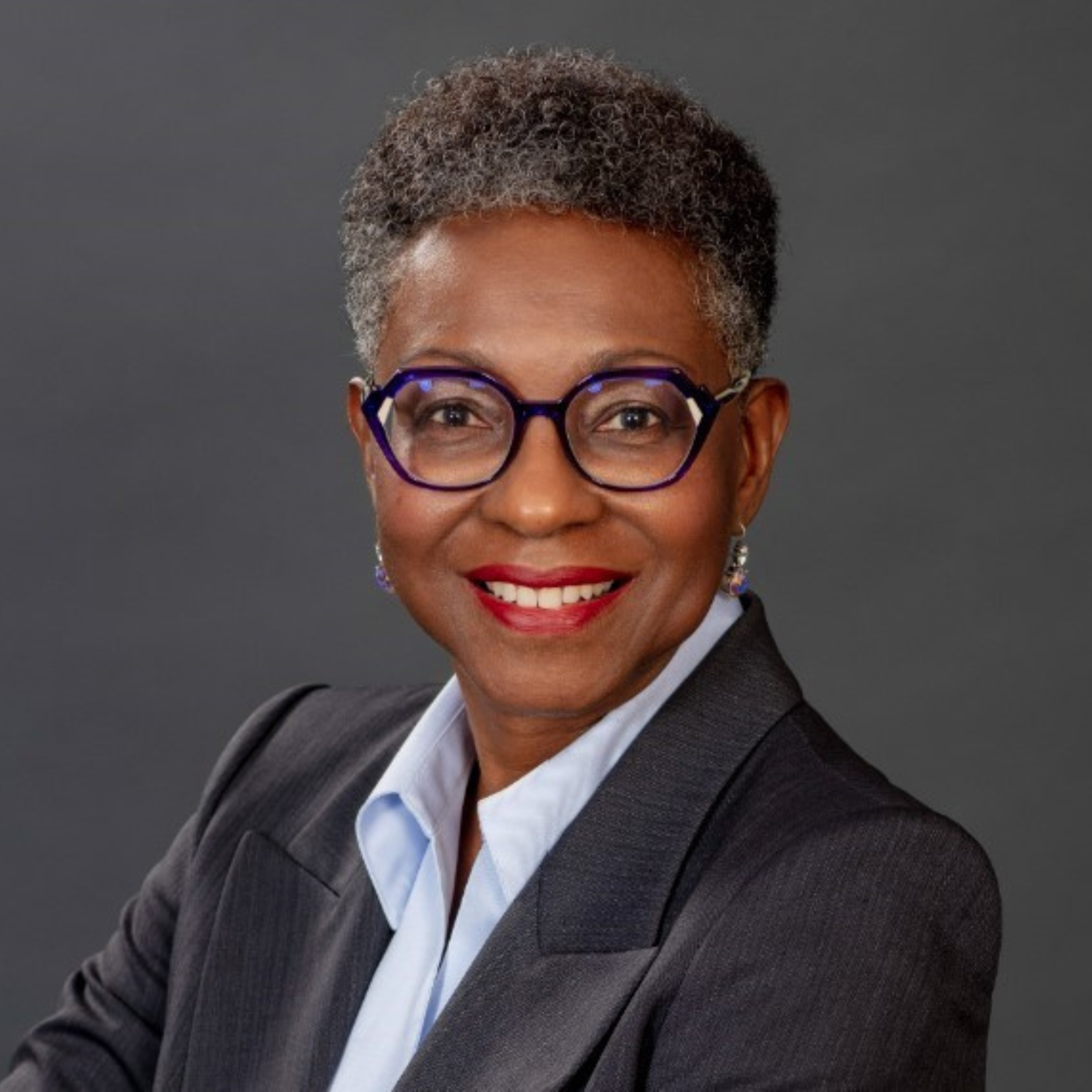 Christine Williams is pictured in professional clothes, smiling for her headshot in front of a grey background.