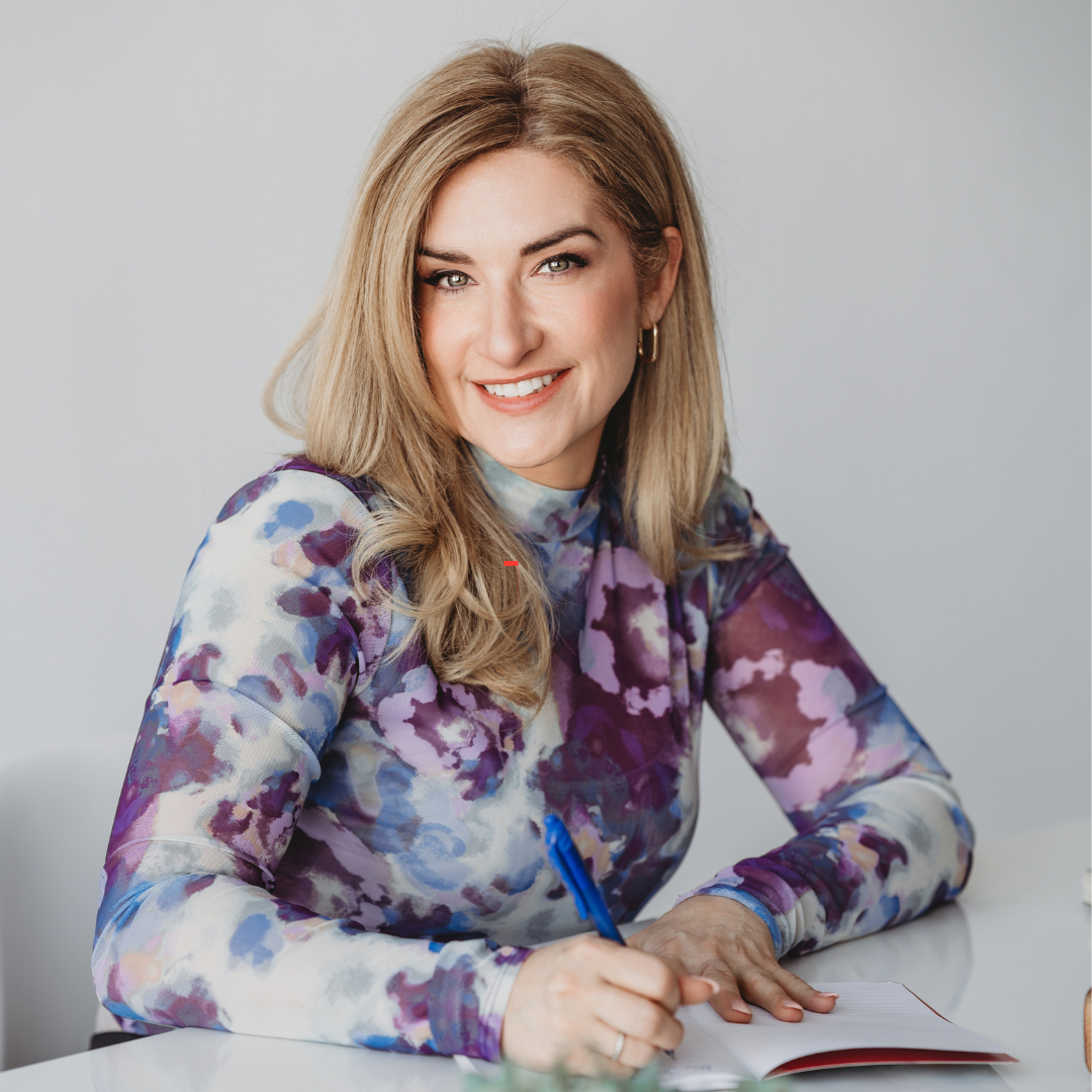 Dr. Maude Champagne is seated at a desk writing in a notebook as she smiles for her headshot.