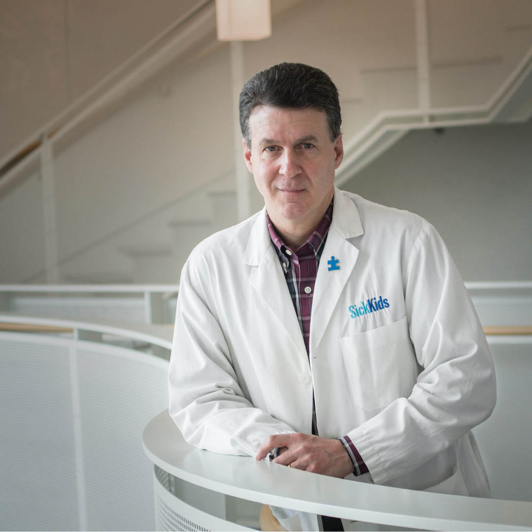 Dr. Steve Scherer is posing for a photo in the Sick Kids building. He is wearing his lab coat and leaning against a balcony. 