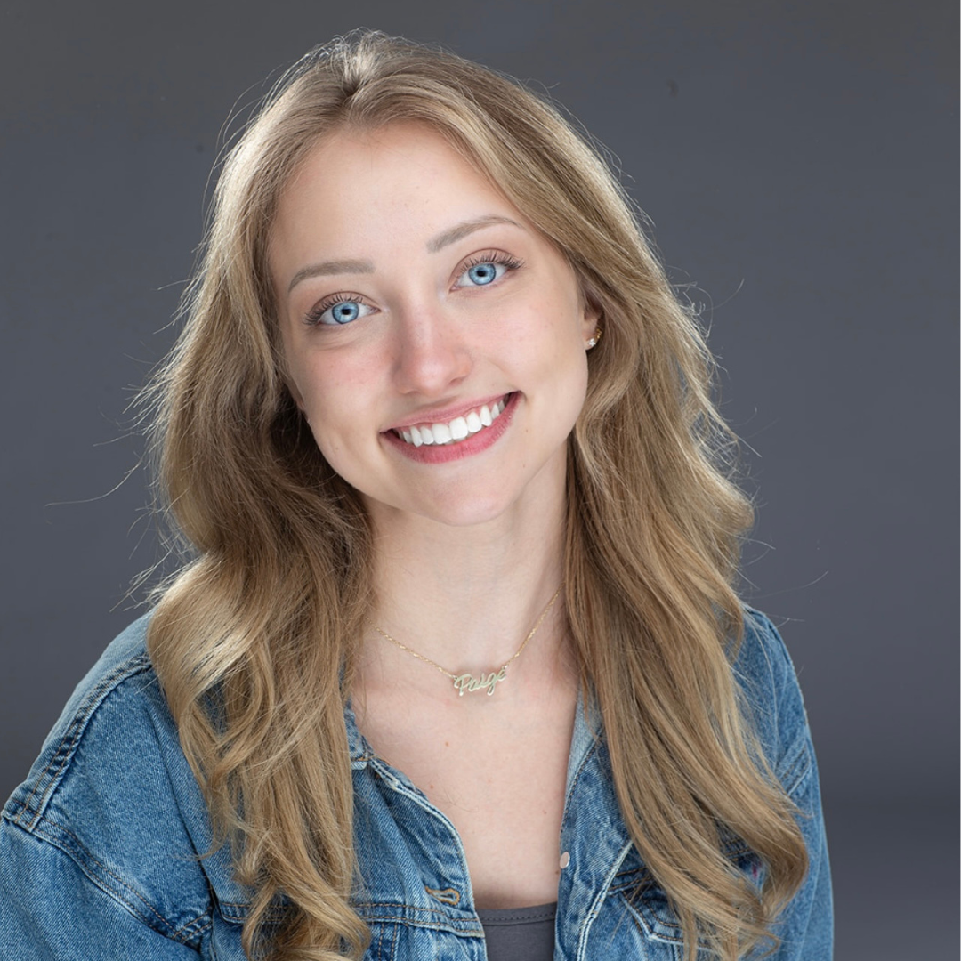 Paige is smiling for her headshot in front of a grey background.