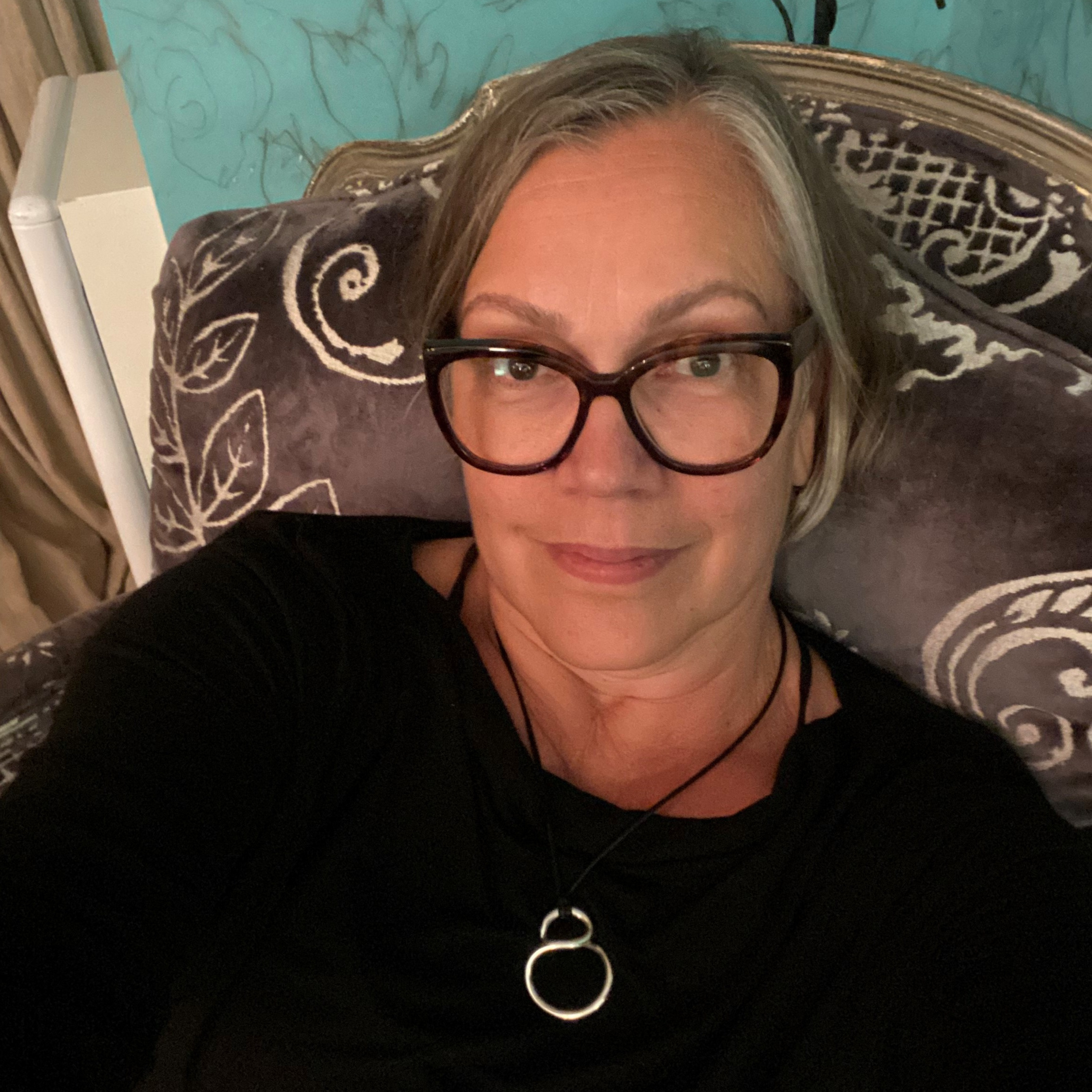 Tina is smiling for a selfie as she sits in a lounge chair in her living room.