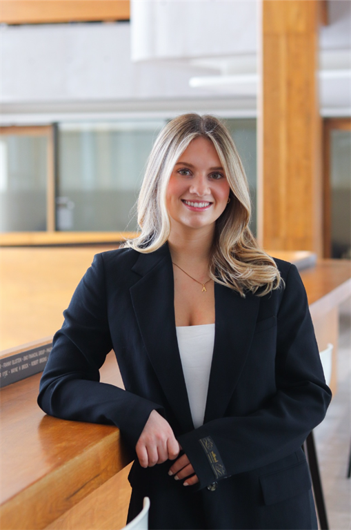 August Hummelbrunner poses smiling while leaning on a balcony wall. She is wearing professional clothes.