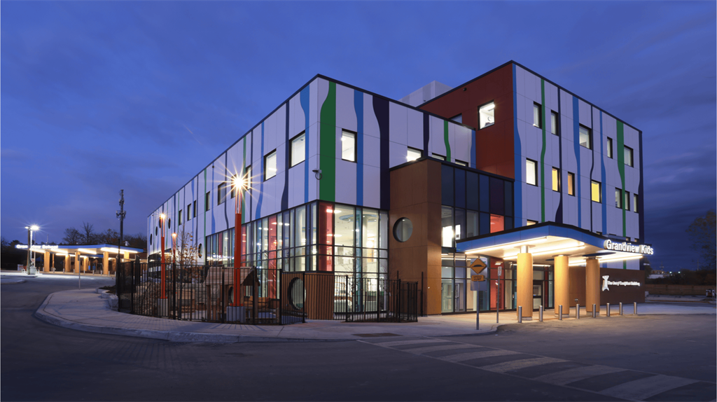 The image shows the new Grandview Kids building at night. The glass and colourful exterior shines from the lights within against the dark sky.