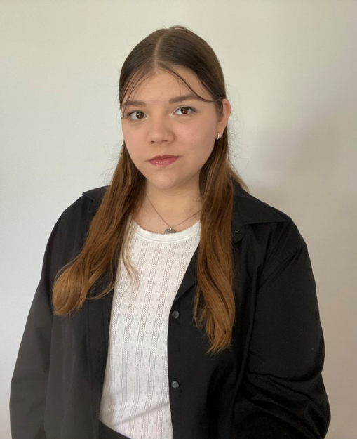 Kim is posing for a photo, she is wearing professional clothing and smiling in front of a blank white wall.